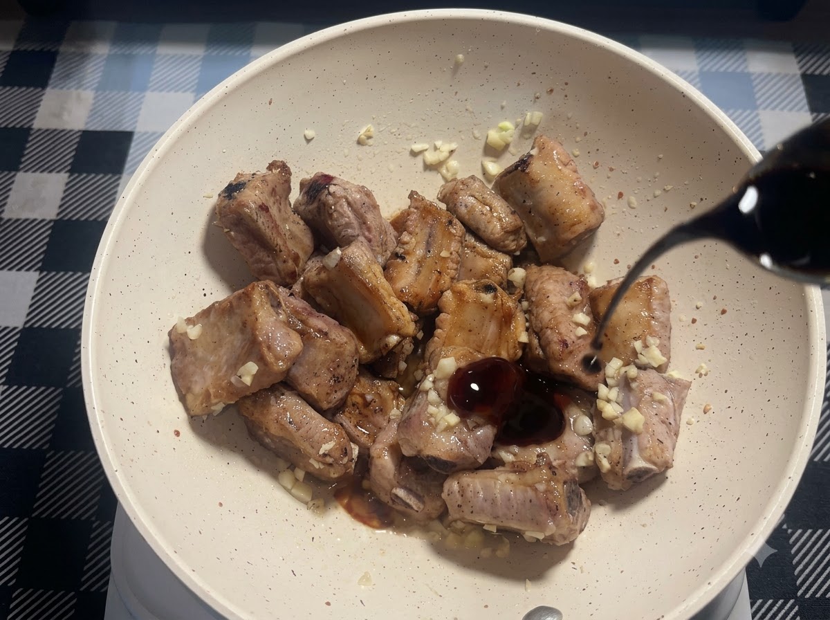 A small stream of dark soy sauce being poured into the pan with fried pork ribs and minced garlic.
