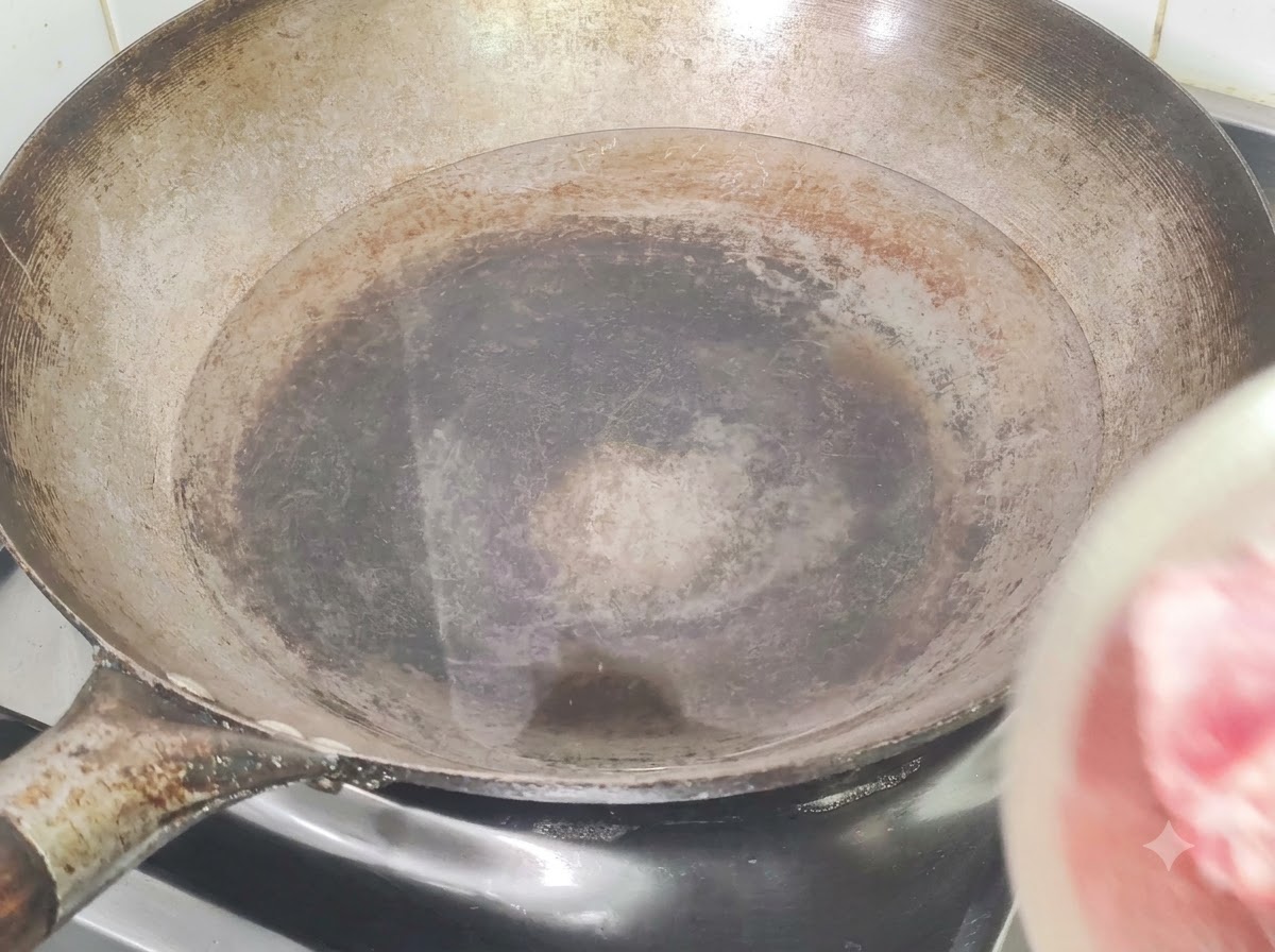 Pork ribs being added to a wok filled with cold water, ginger, and cooking wine for blanching.