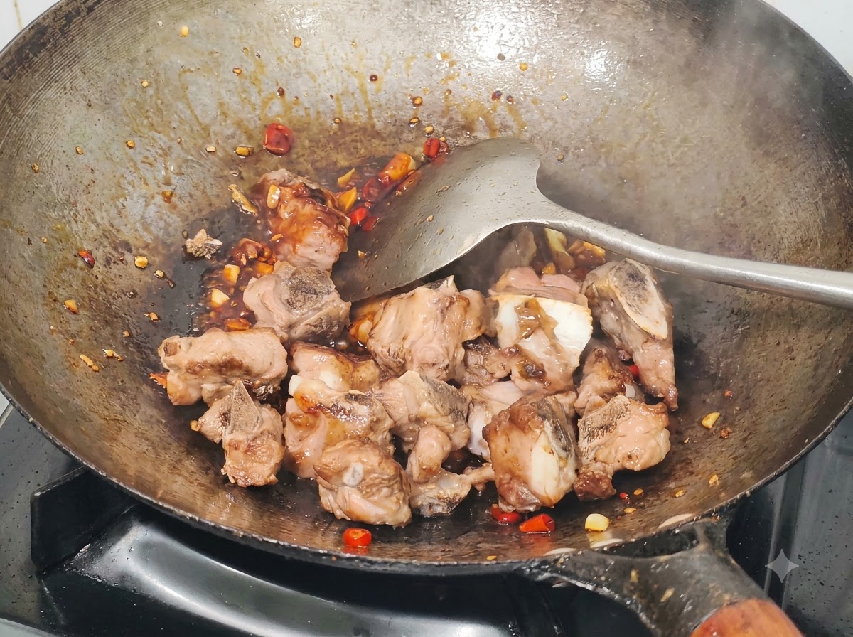 Fried pork ribs being tossed in a wok with sauce, chopped millet peppers, and garlic using a metal spatula.