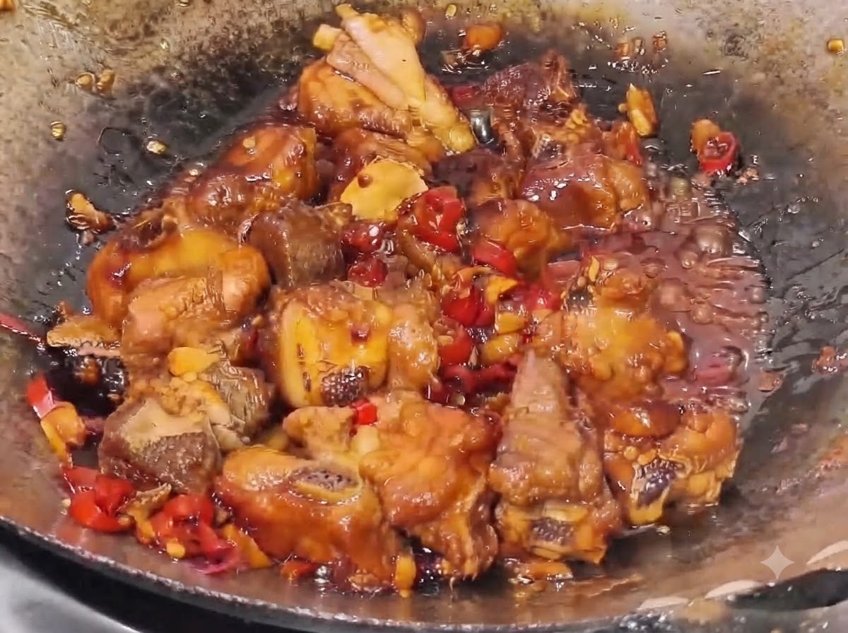 Pork ribs simmering in a thick, dark sauce with visible bits of red chili and garlic pieces in a wok.