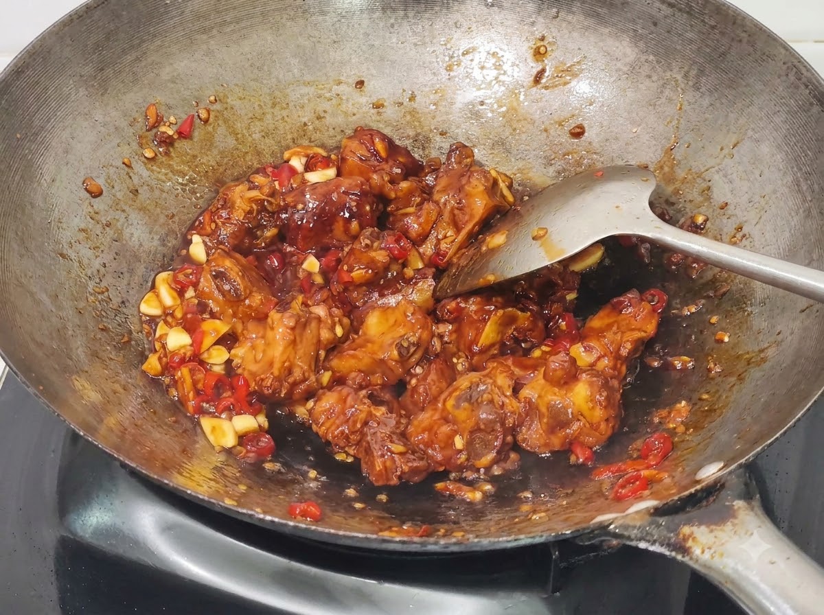 Chopped green onions being mixed into the cooked honey garlic pork ribs in the wok.