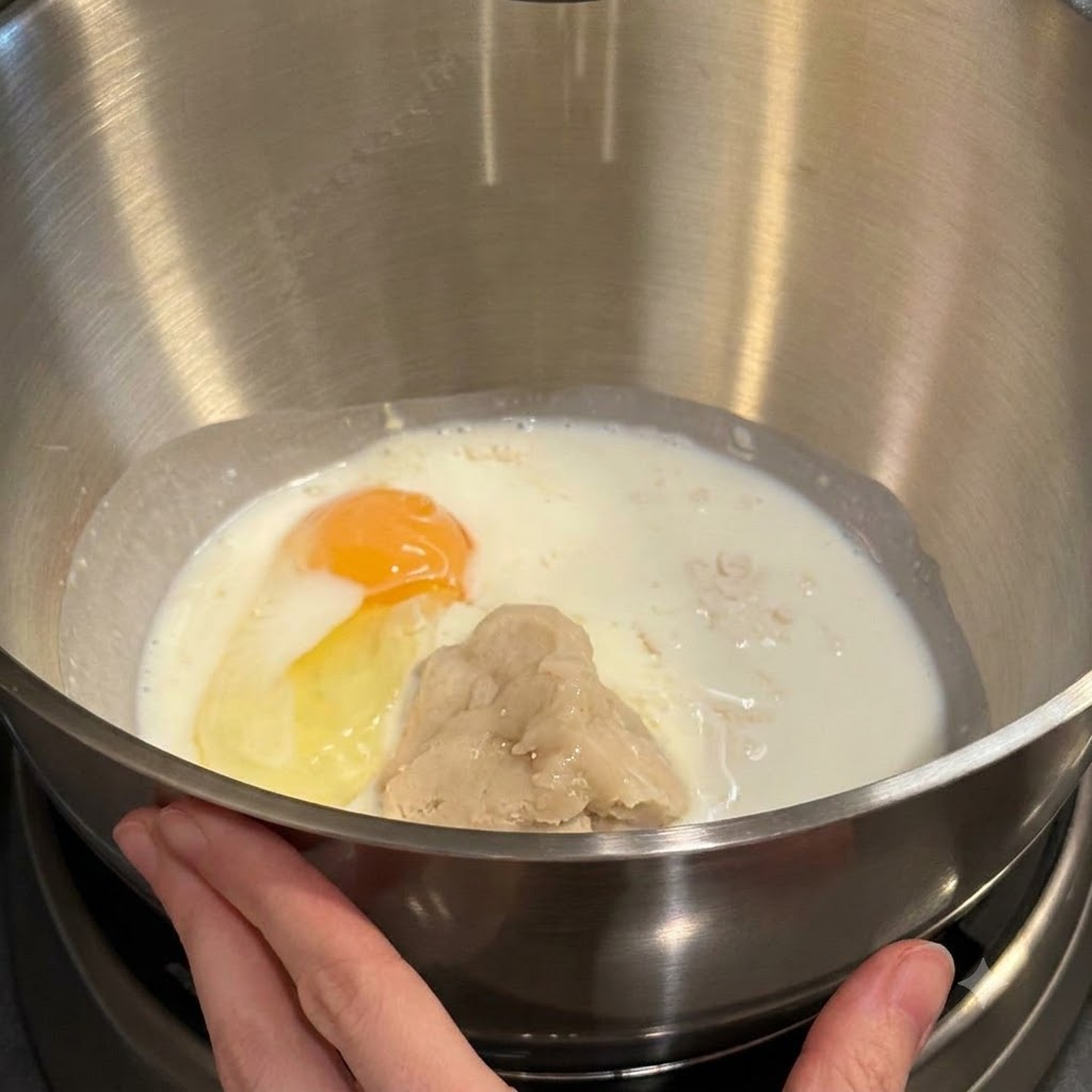Mixer bowl containing flour, milk, an egg yolk, and tangzhong paste ready for mixing.