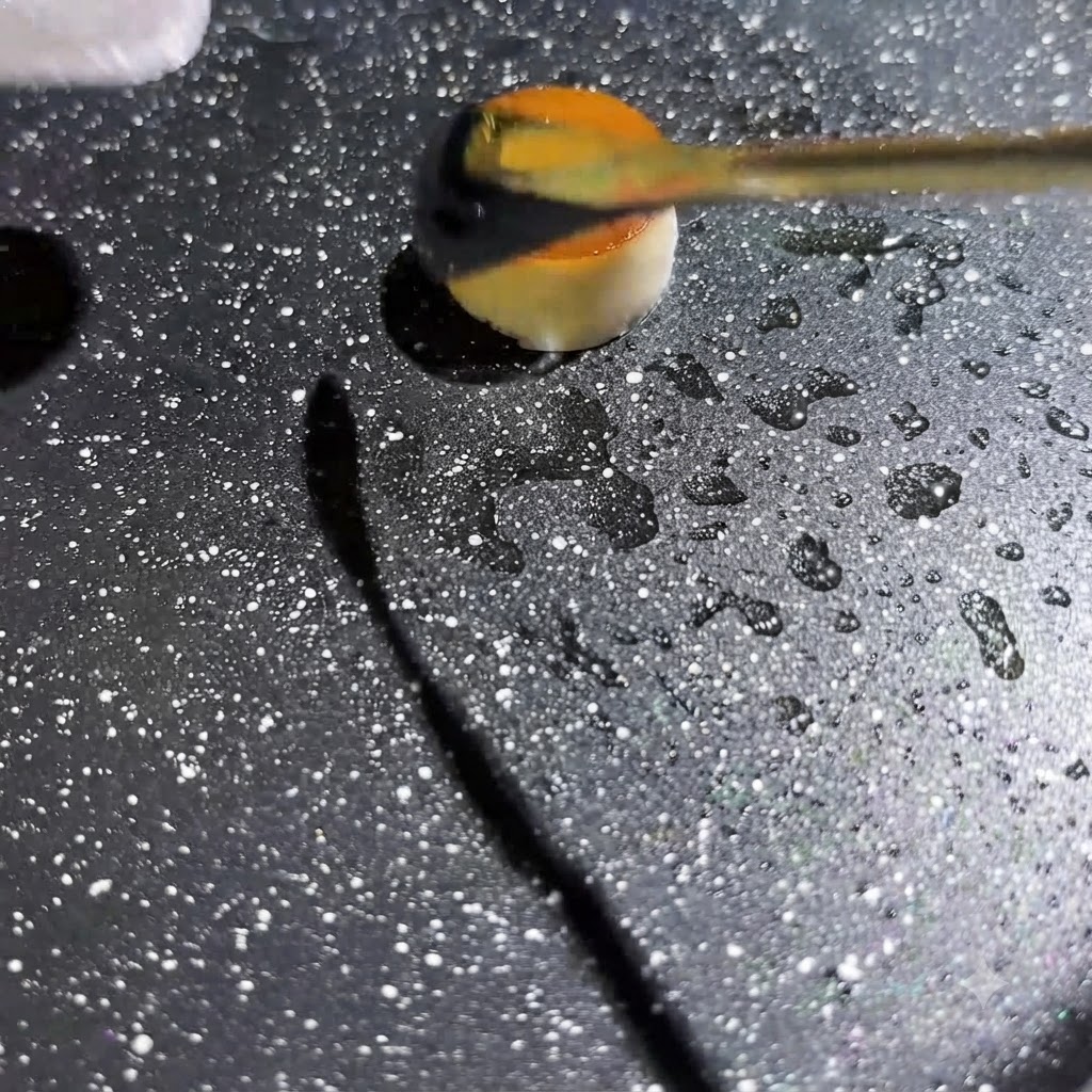 Yellow egg liquid being squeezed into the center of a small hollow mushroom ring in a hot, speckled pan.