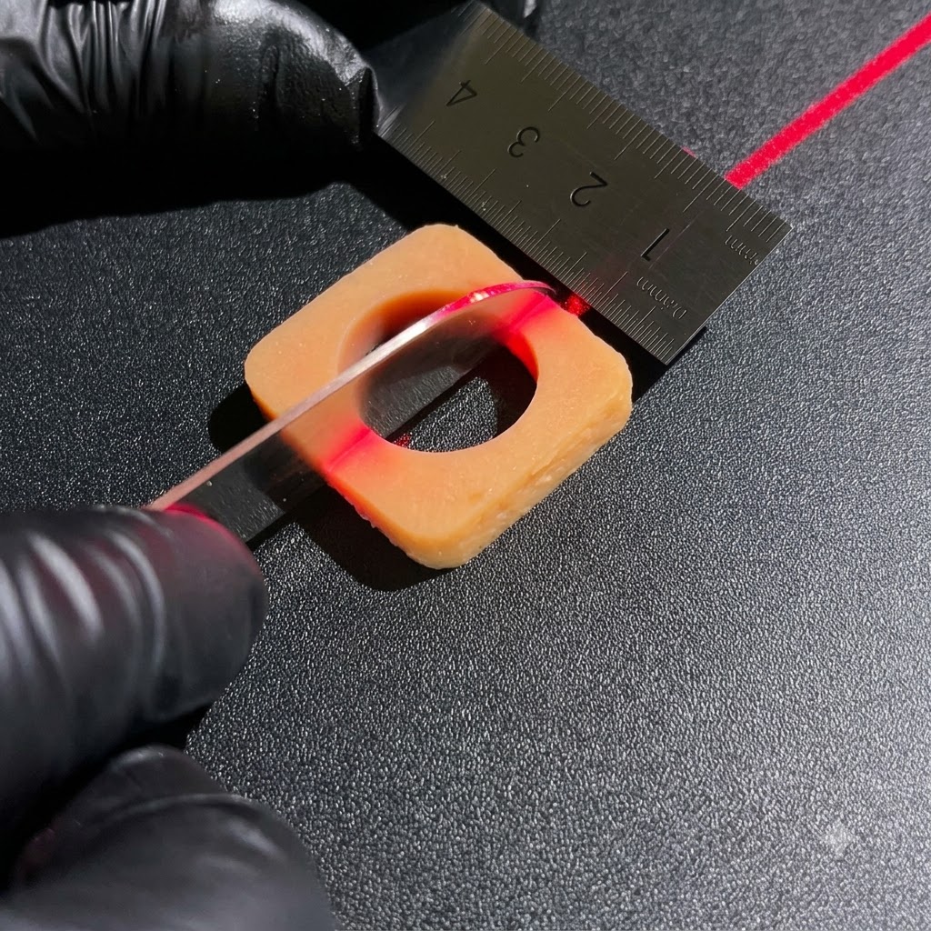 Gloved hands using a sharp knife and metal ruler to cut square ingredient blocks under a red laser alignment line.