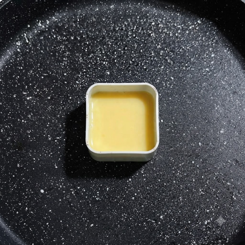 A square metal mold filled with yellow egg liquid resting in the frying pan, ready for ingredient placement.