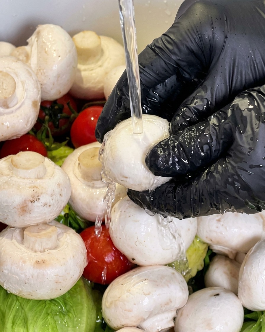 A white mushroom being rinsed under running water.