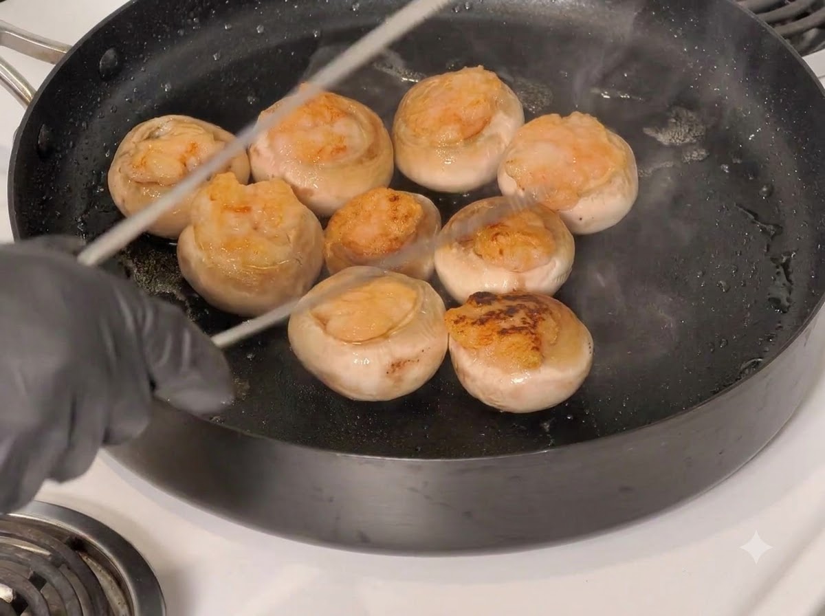Stuffed mushroom caps being turned over in the frying pan using tongs.