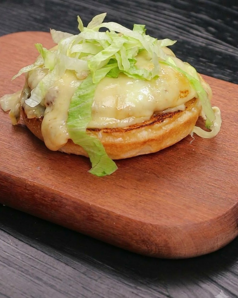 Fresh shredded lettuce piled neatly over a melted cheese and beef patty resting on a toasted bun base.
