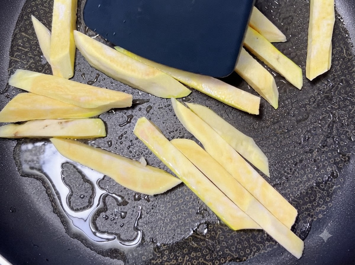 Raw sweet potato sticks sizzling in a heated black pan with oil while being moved with a spatula.