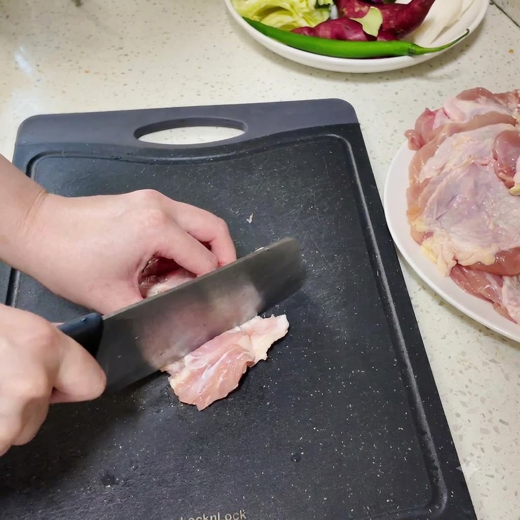 Boneless chicken drumsticks being chopped into smaller pieces on a black cutting board.