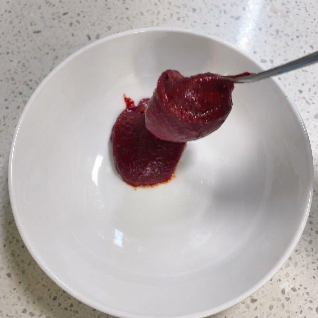 Korean chili paste and other seasonings being stirred inside a white bowl.