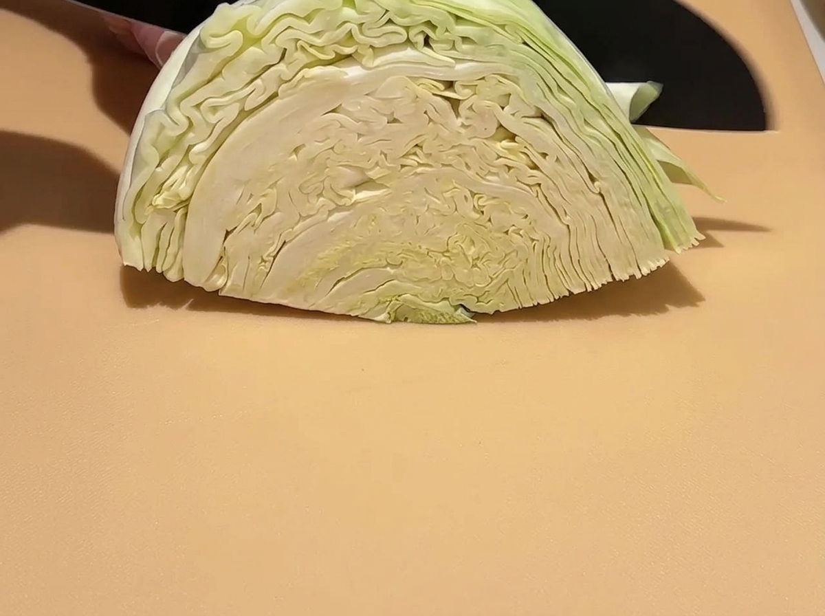 A wedge of raw green cabbage being sliced into smaller pieces on a cutting board with a knife.