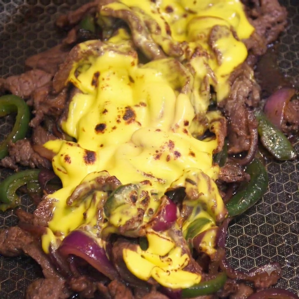 A kitchen flame torching the melted yellow cheese topping on the beef mixture in a pan.