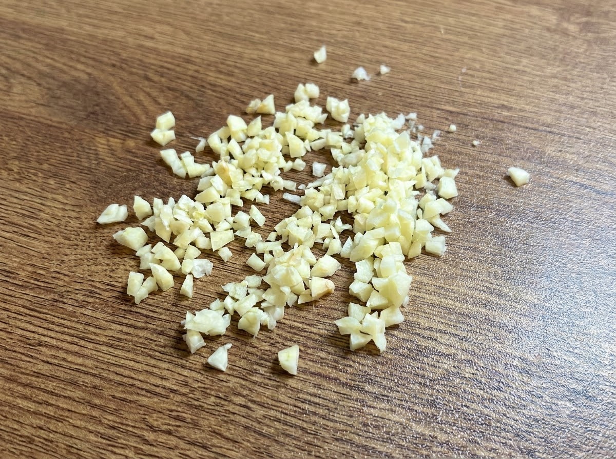 A small pile of finely minced fresh garlic resting on a wooden cutting board.