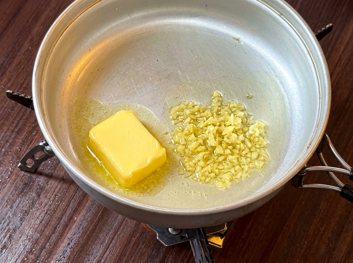 A slice of yellow butter melting down in a metal pan on a camping stove.