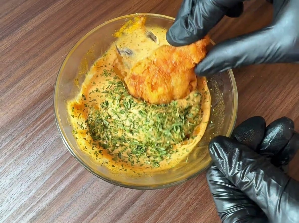 Freshly chopped parsley being sprinkled over a bowl of prepared burger sauce as a fried food piece is dipped into it.