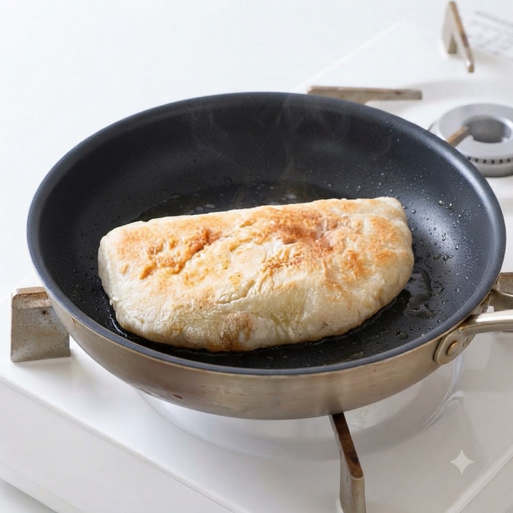 Ciabatta bread halves frying in oil inside a pan until golden and crispy.
