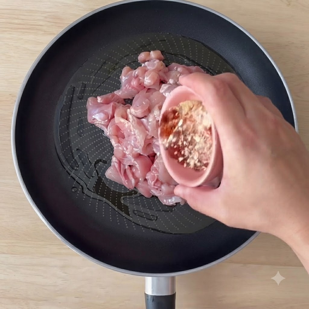 Boneless chicken pieces cooking in a pan with olive oil and spices being stirred.