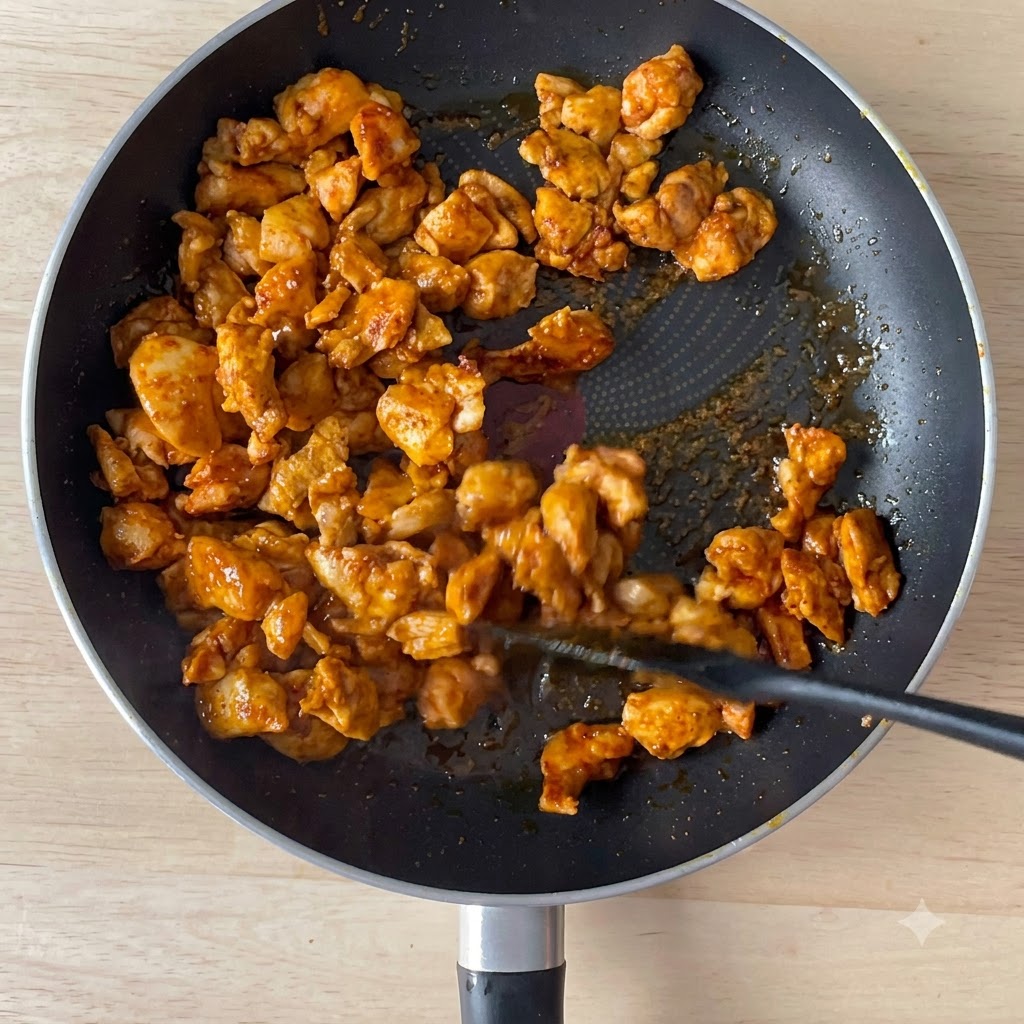 Soy sauce being poured into a pan with browned chicken chunks.