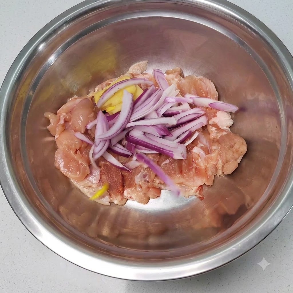 Raw chicken pieces mixed with sliced red onions and ginger inside a stainless steel mixing bowl.