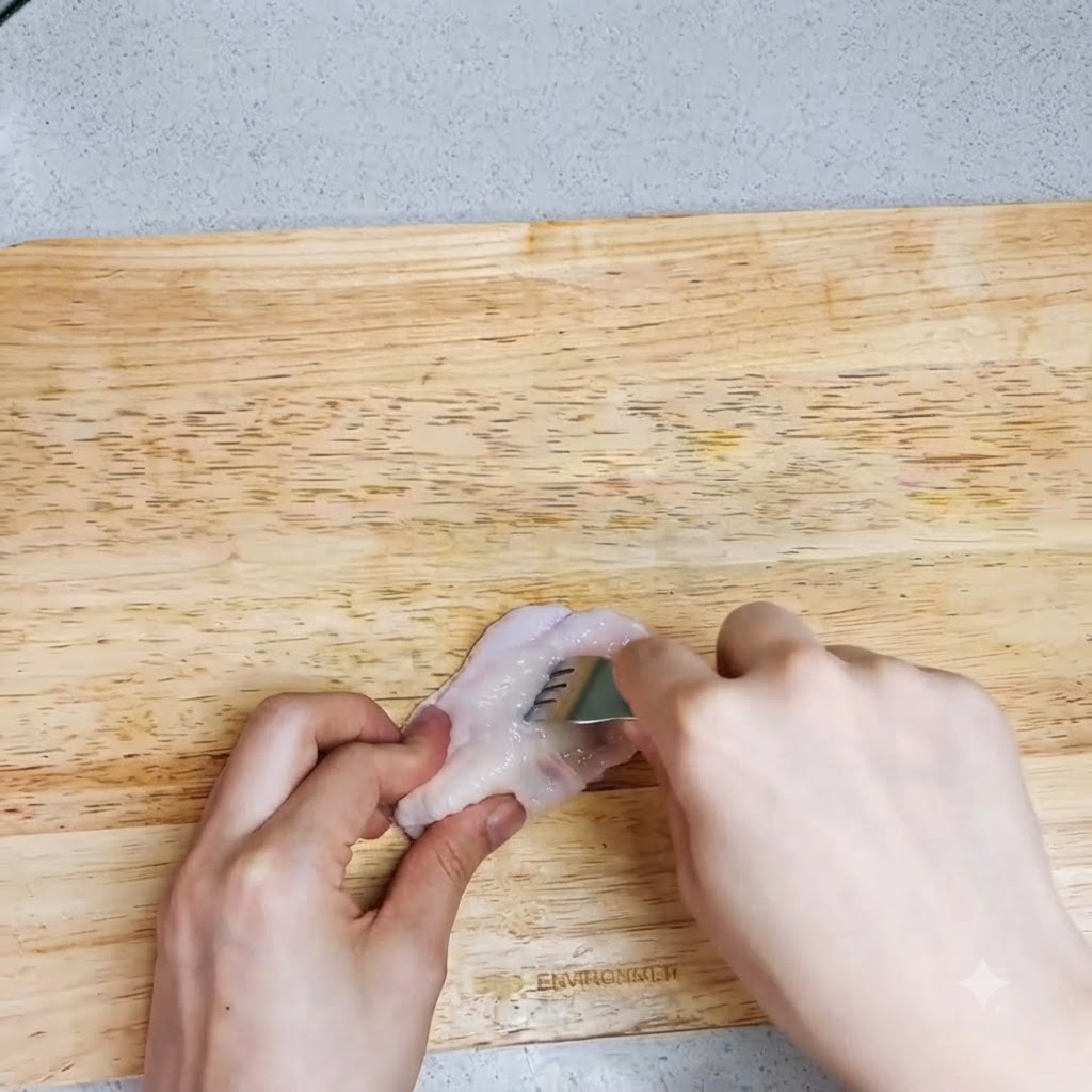 A pair of hands using a fork to poke holes into a raw chicken wing on a cutting board.