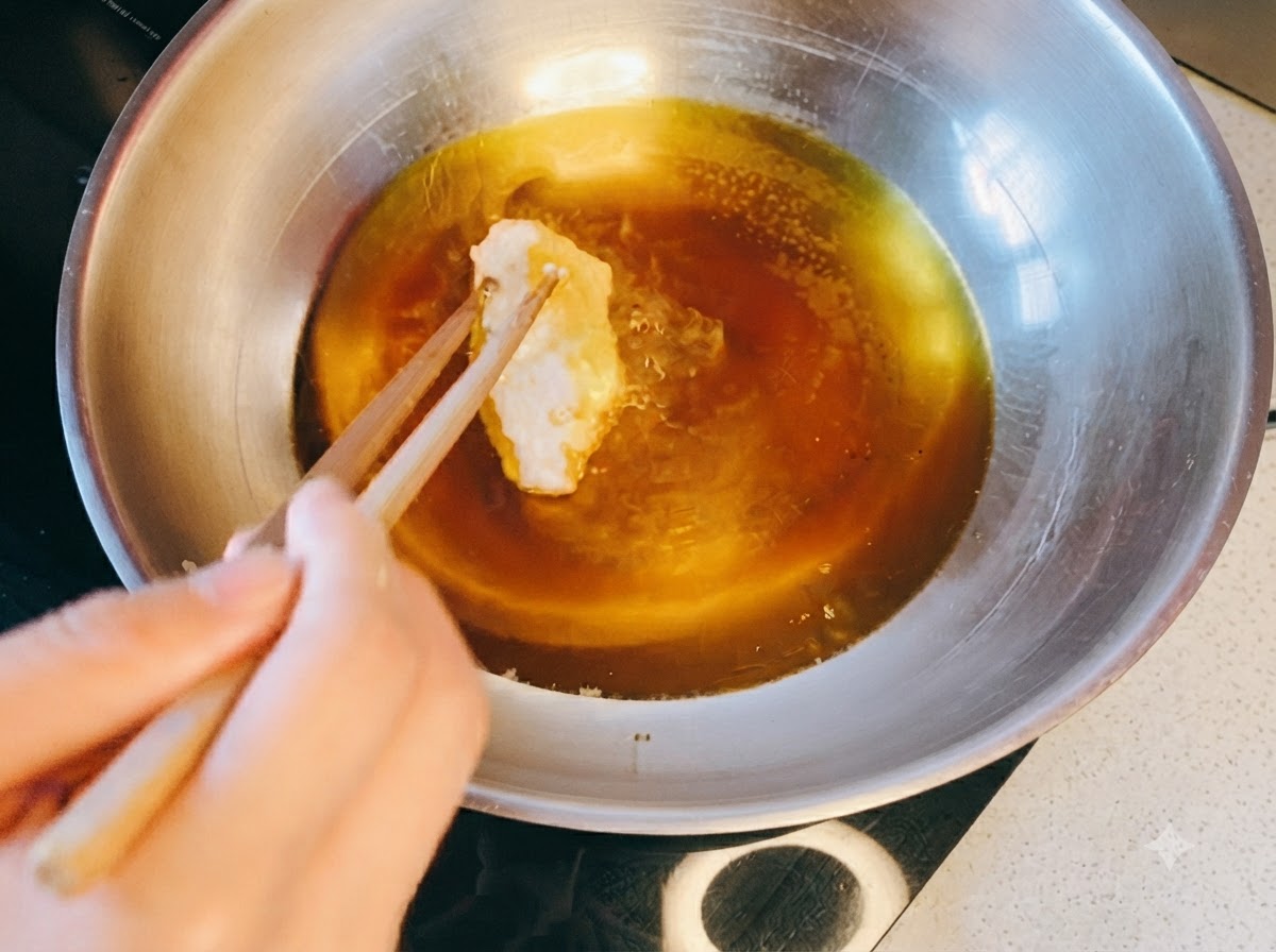 Chopsticks placing a breaded chicken piece into a metal pan filled with hot oil.