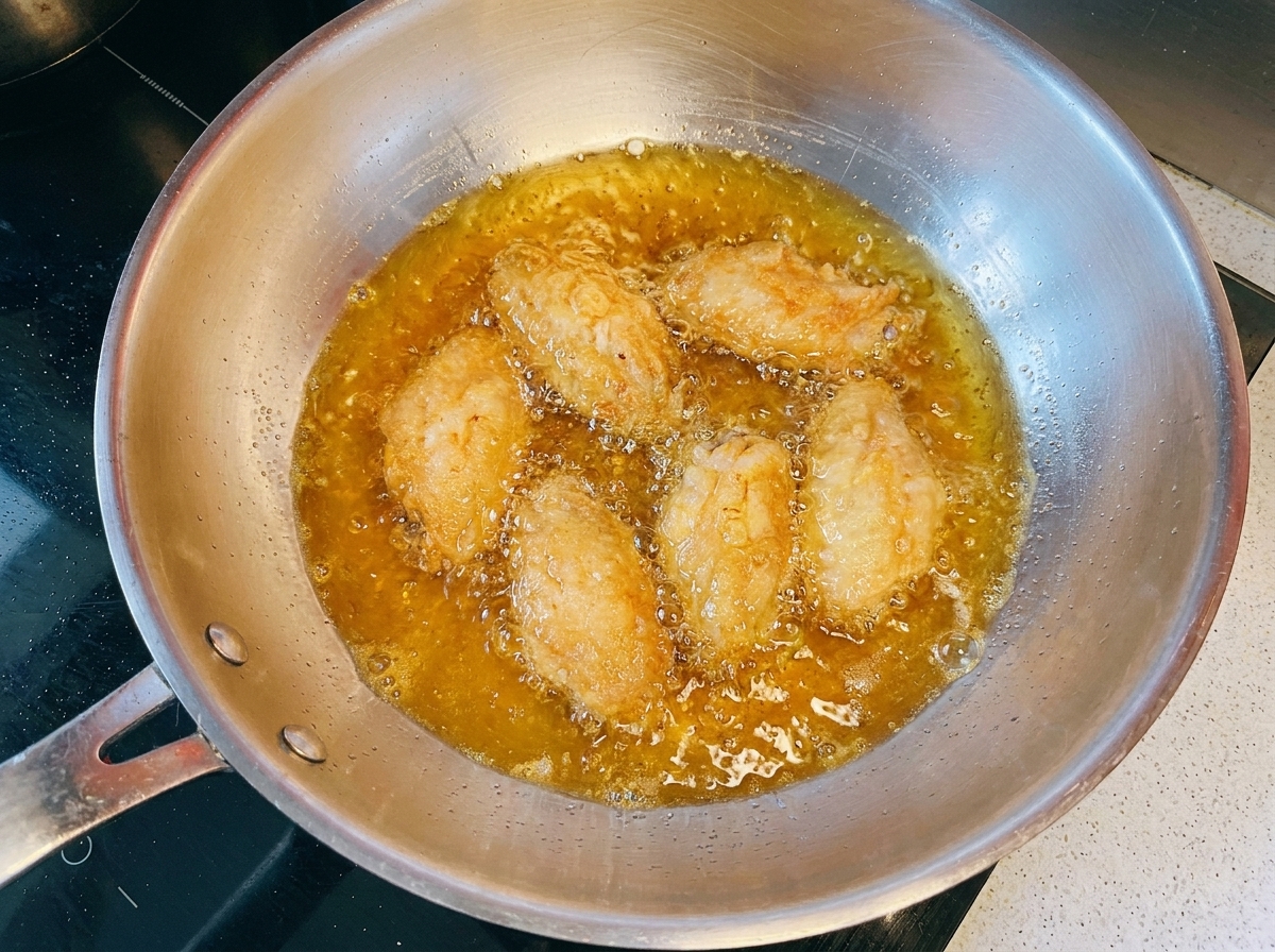 Golden-brown chicken wings frying in hot oil inside a metal pan.