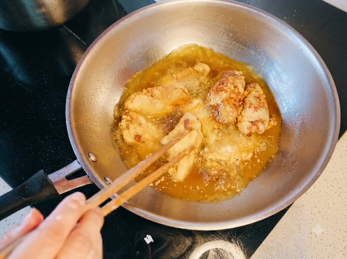 Chicken wings being stirred and double-fried in hot oil with chopsticks.