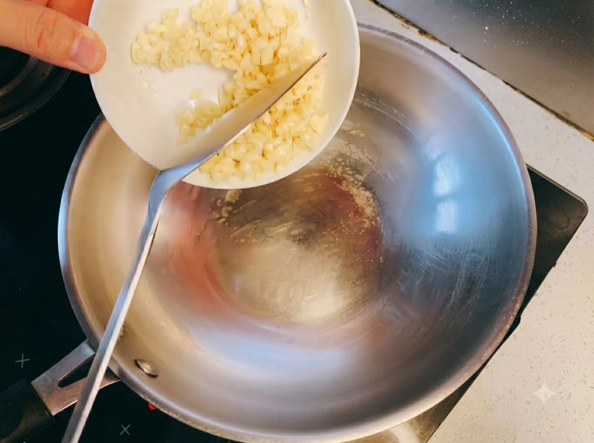 Minced garlic hitting hot oil in a stainless steel wok and beginning to sauté.