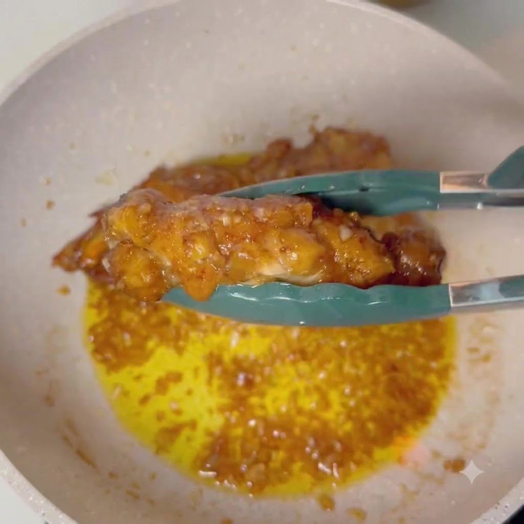 Tongs holding a glazed chicken drumstick over a pan of bubbling garlic butter sauce.