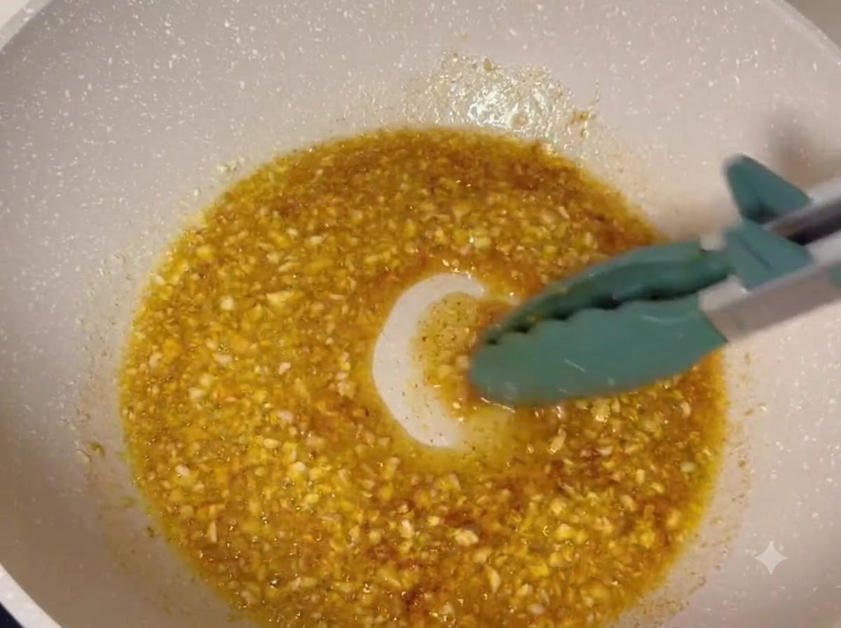 Fried chicken drumsticks being tossed in a bubbling garlic butter glaze inside a pan.