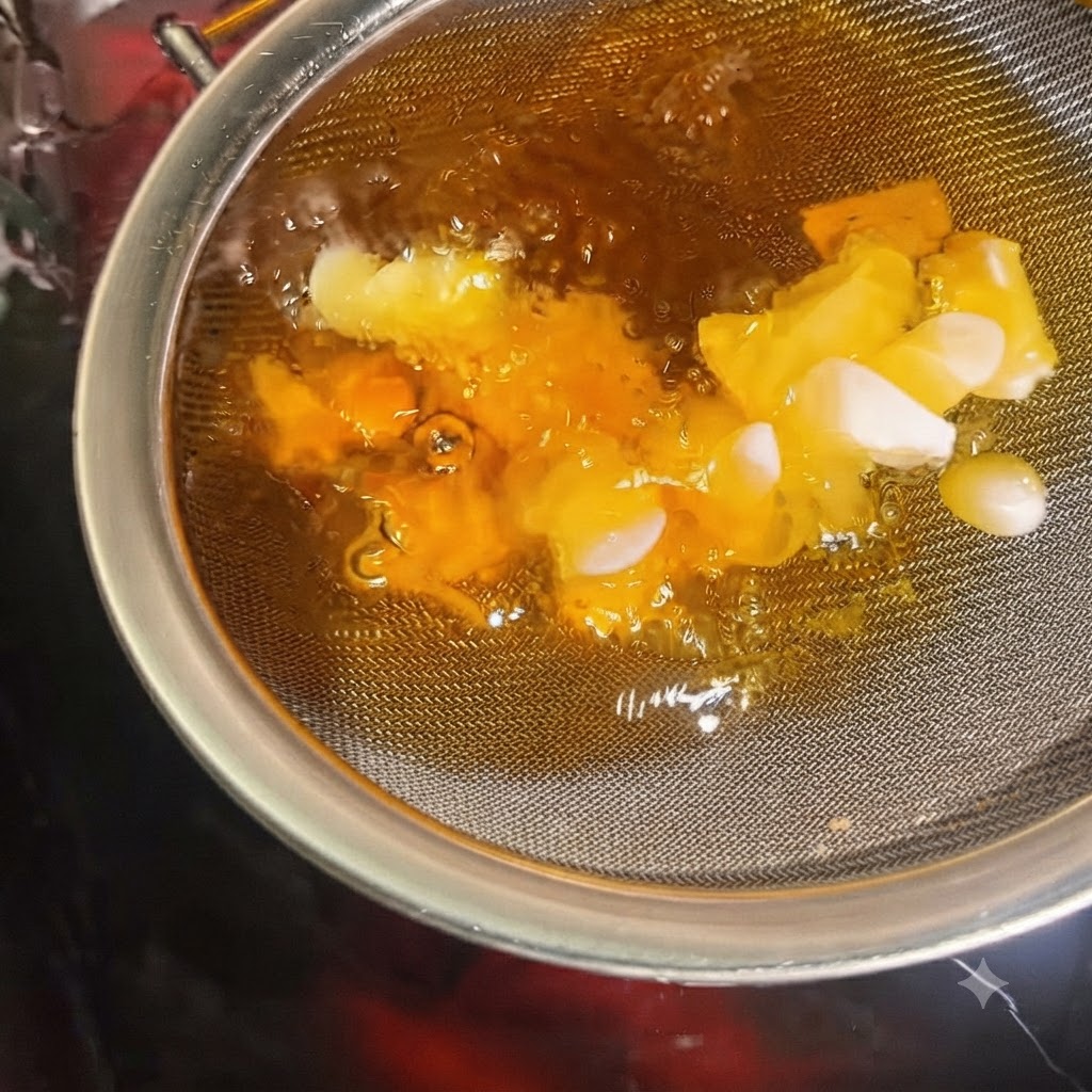 Garlic slices crisping and turning golden inside a strainer submerged in hot oil.