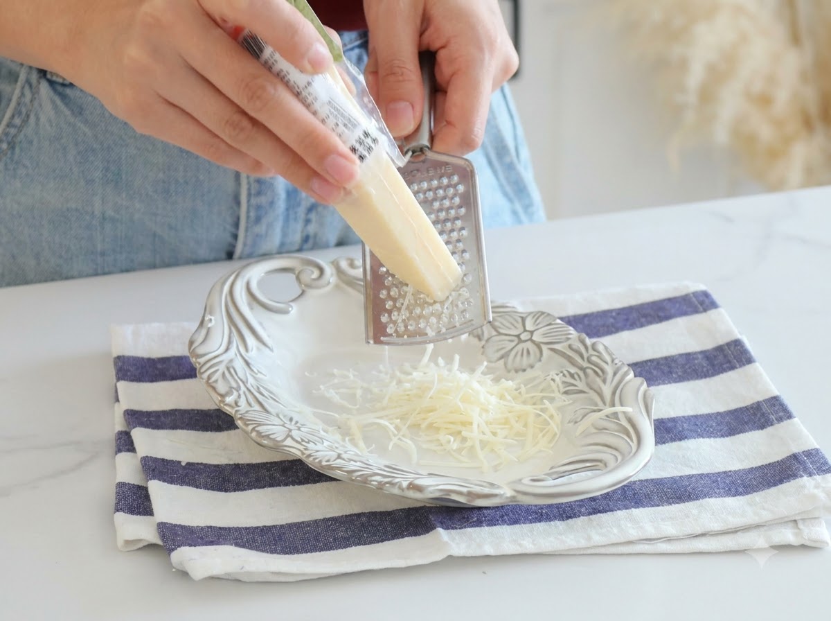 Parmesan cheese being freshly grated with a metal grater onto a white plate.